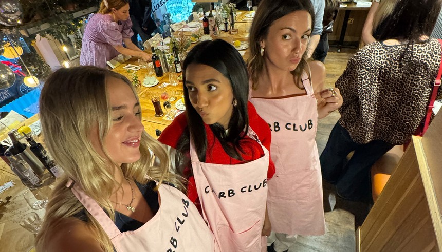 Three women in aprons collaborating in a lively restaurant, showcasing teamwork and culinary passion.